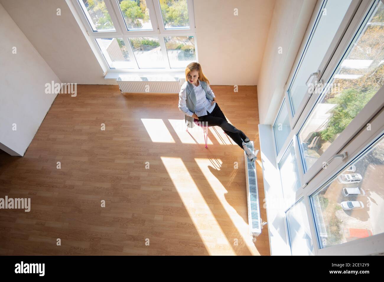 Blick von oben auf ein großes Zimmer mit großen Fenstern, wo ein Mädchen auf einem Stuhl sitzt Stockfoto