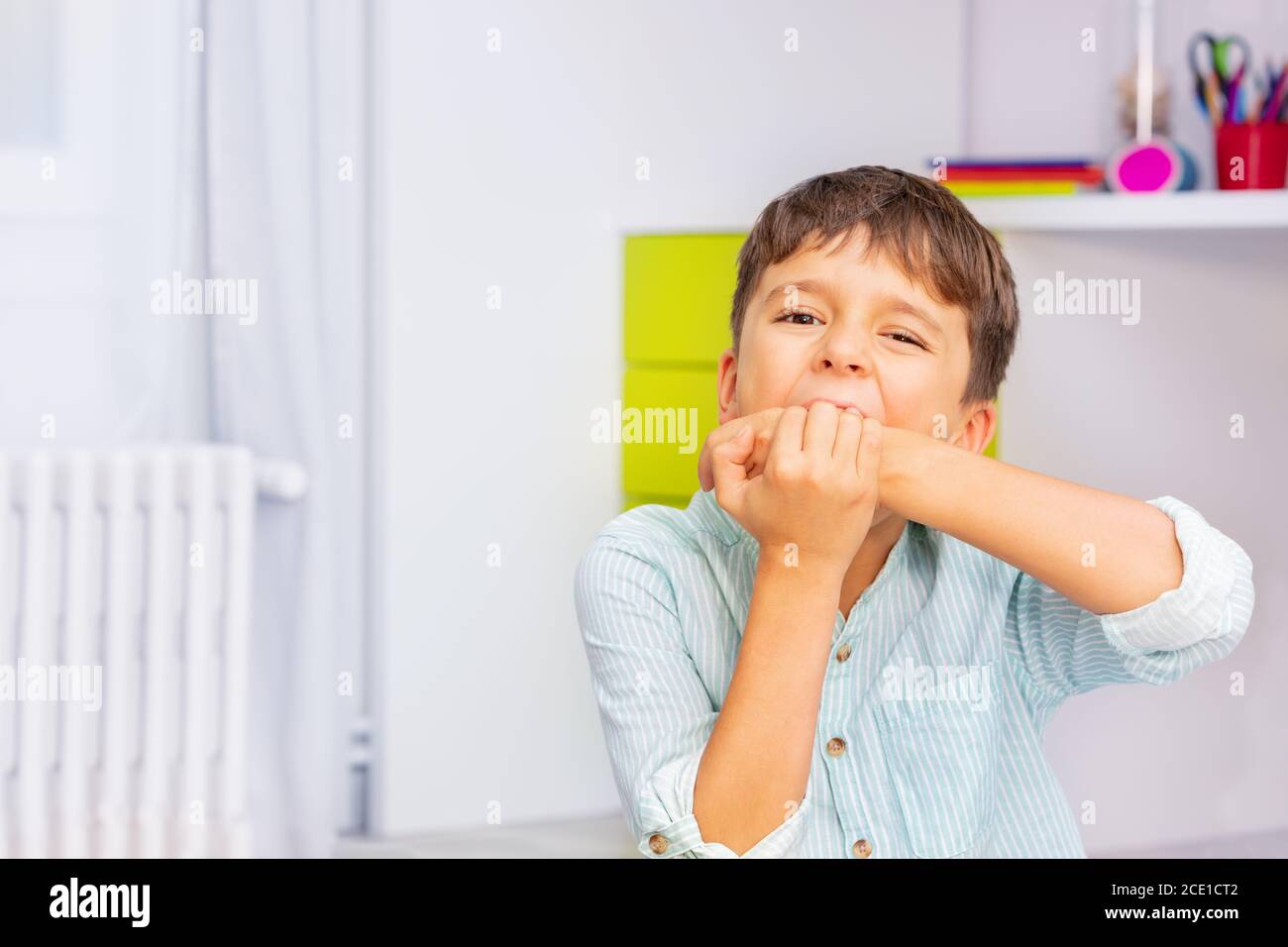 Close Portrait von kleinen autistischen Jungen beißen Hände mit starken negativen Gesichtsausdruck sitzen in seinem Zimmer, Selbstverletzung Problem Stockfoto