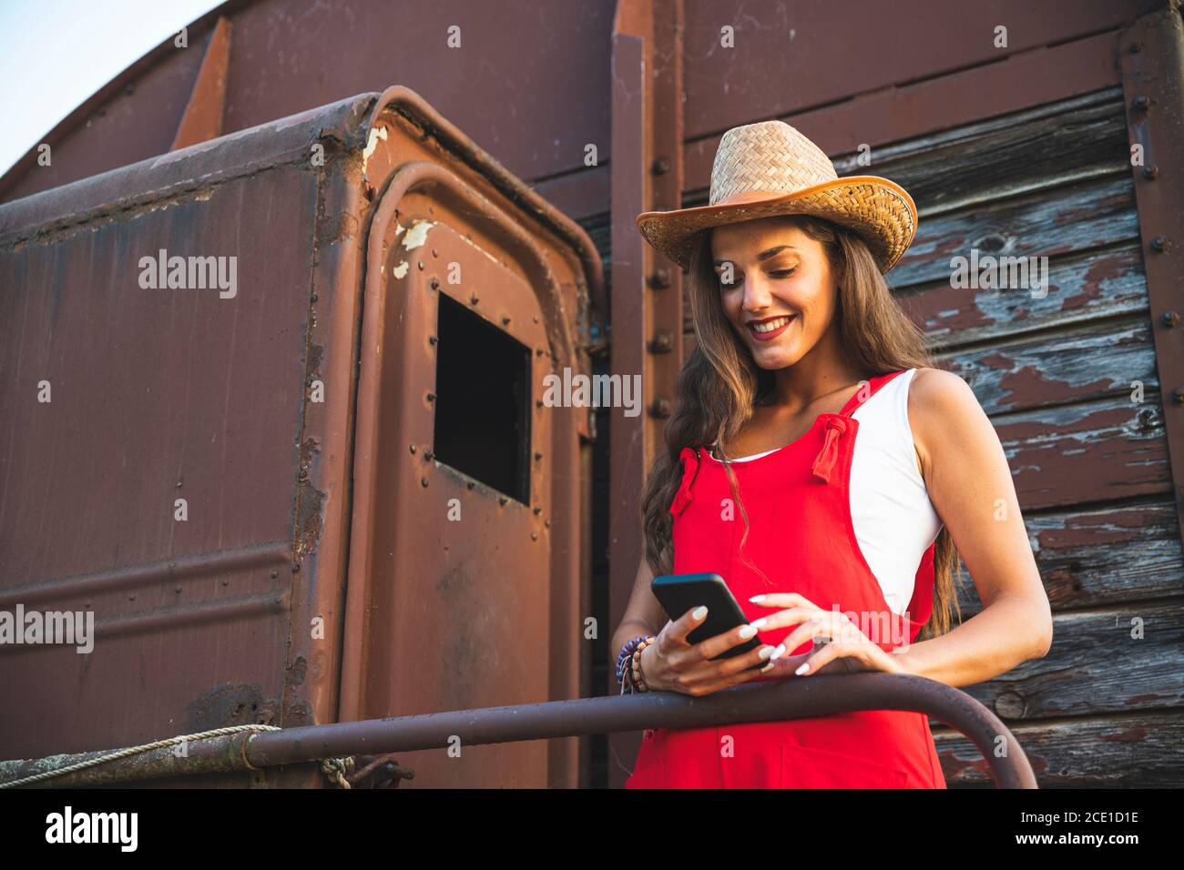 Schöne junge Mädchen lächelnd und mit Smartphone für Texting ath die Rückseite eines alten Vintage Zug Wagon. Ranch Konzept Fotografie Stockfoto
