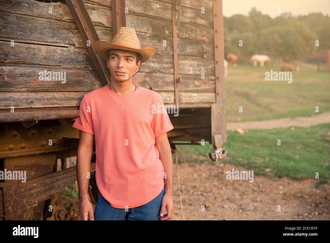 Porträt eines jungen Mannes mit Jeans und einem Cowboy Hut vor einem hölzernen Wagen in der Ranch. Ranch Konzept Fotografie Stockfoto