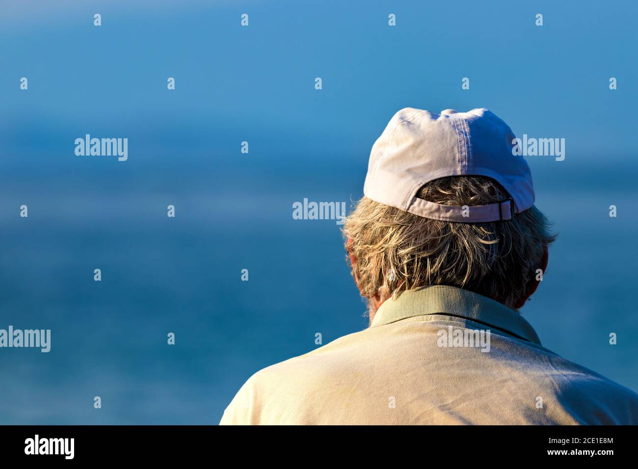 Nahaufnahme des Rückens eines älteren Mannes Kopf mit grauen Haaren trägt eine Tasse Blick auf das Meer Stockfoto