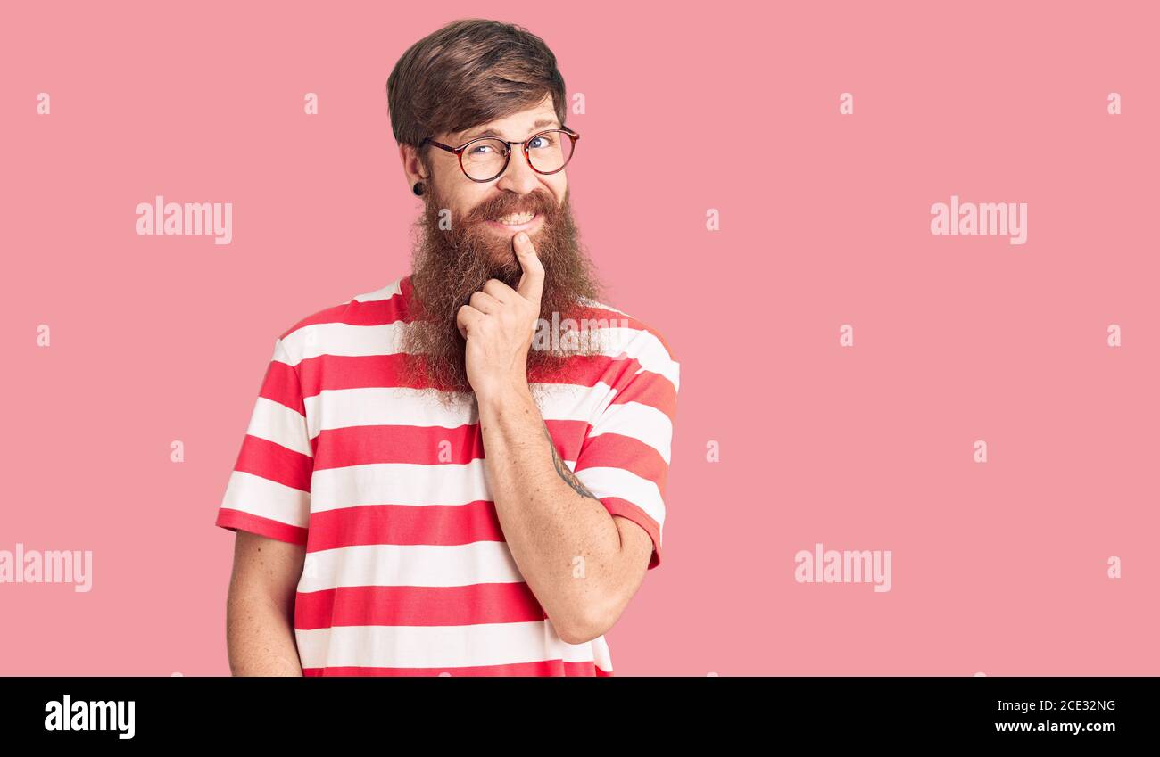 Hübscher junger Mann mit rotem Kopf und langem Bart, der lässig getragen wird Kleidung, die selbstbewusst auf die Kamera schaut, mit einem Lächeln mit gekreuzten Arme und Hand auf Chi angehoben Stockfoto