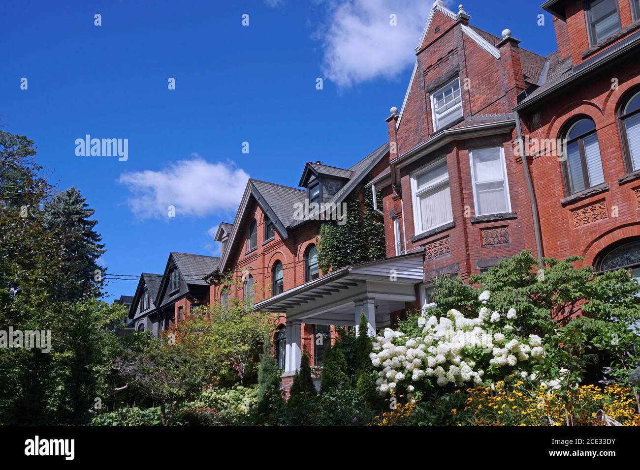 Straße von alten Doppelhaushälften mit Giebeln und Sommerblumen In üppigen Gärten Stockfoto