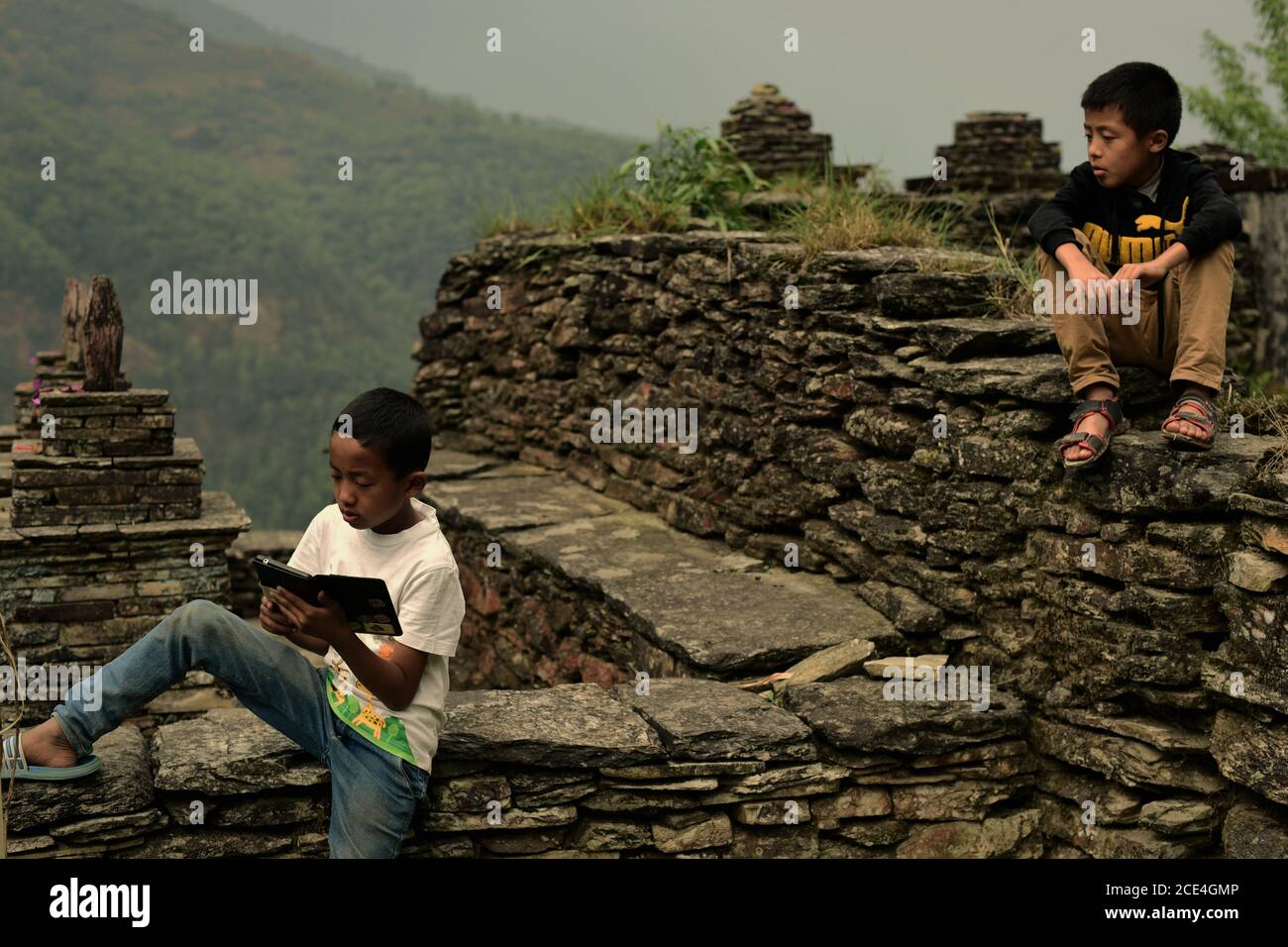 Ein Teenager, der einen Tablet-Computer in einem Kulturdenkmal im landwirtschaftlichen Dorf Sidhane in der Panchase-Bergregion in Nepal benutzt. Stockfoto