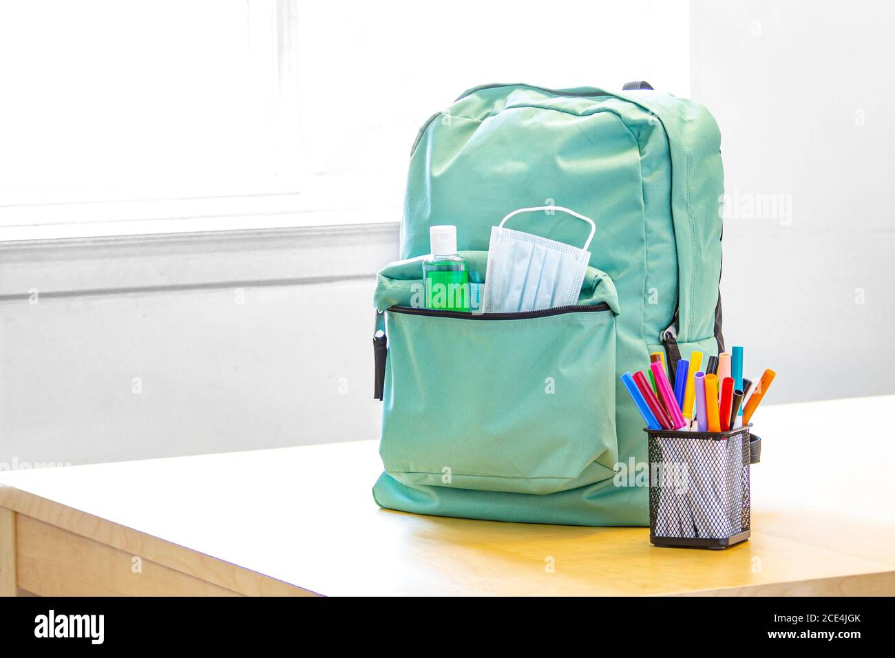 Eine Schultasche mit Desinfektionsmittel und einer Gesichtsmaske und Bleistiftmarkierungen auf einem Tisch. Zurück zur Schule während der globalen Pandemie. Covid 19. Stockfoto