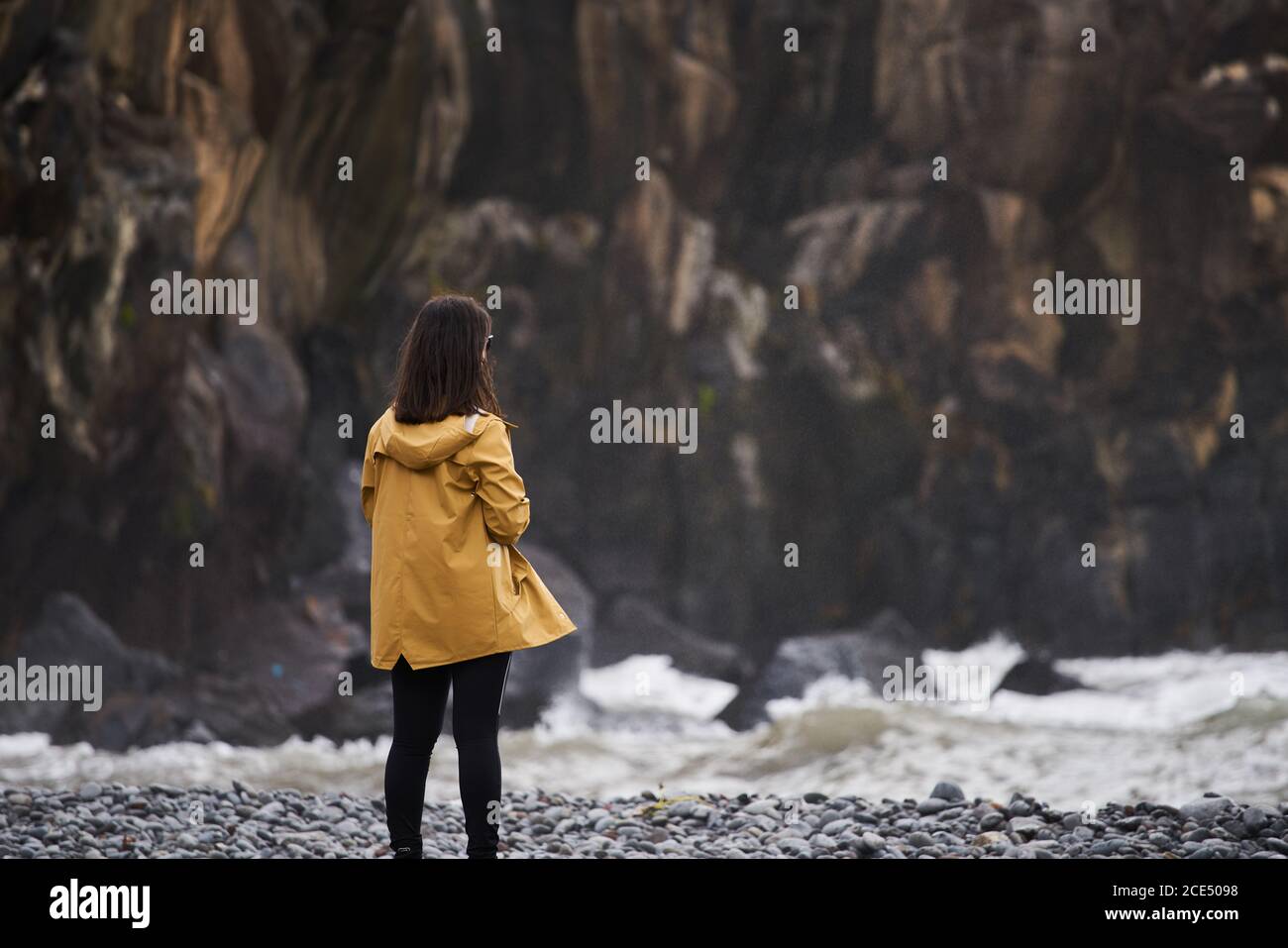 Frau auf eine gelbe Regenjacke mit Blick auf das Meer mit den Felsen, auf dem Hintergrund, in Madeira Stockfoto