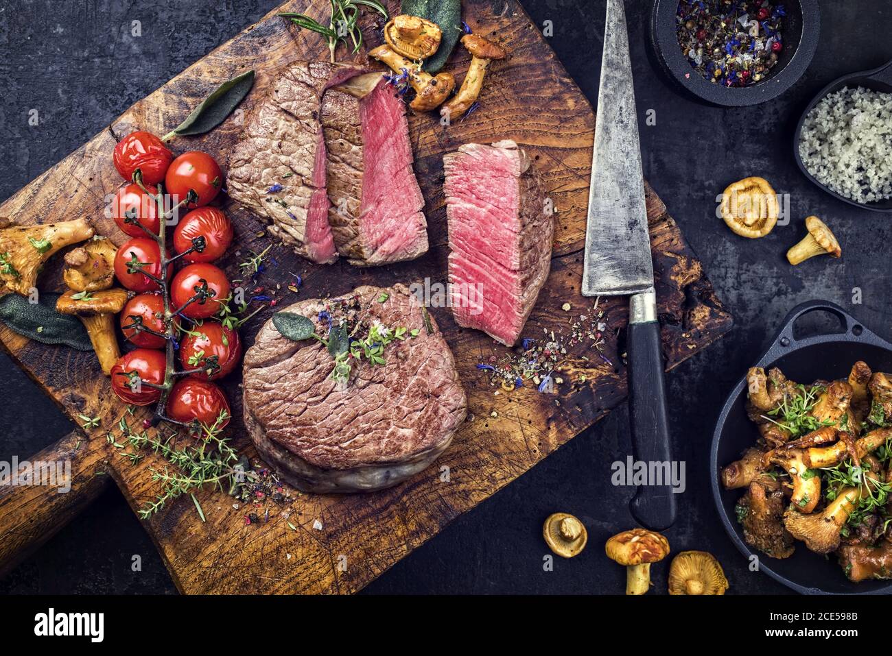 Gebratenes trockenes Rinderfilet Medaillon Steak natürlich mit Tomaten Und Kräuter als Draufsicht auf einem hölzernen Schneidebrett Stockfoto