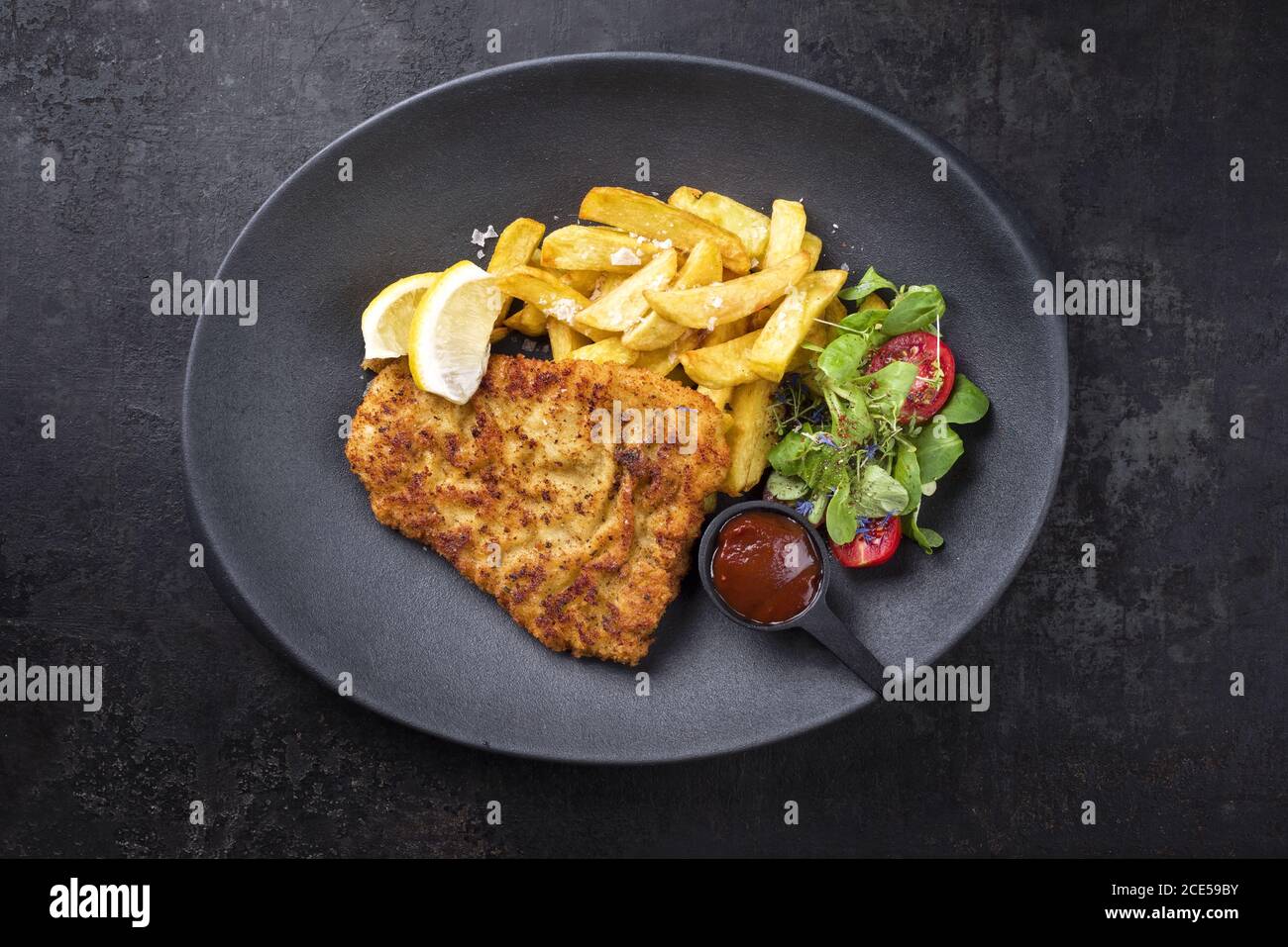 Frittierte Wiener Schnitzel aus Kalbsoberseite mit Pommes frites Und Salat als Draufsicht auf einem modernen Design-Teller Stockfoto