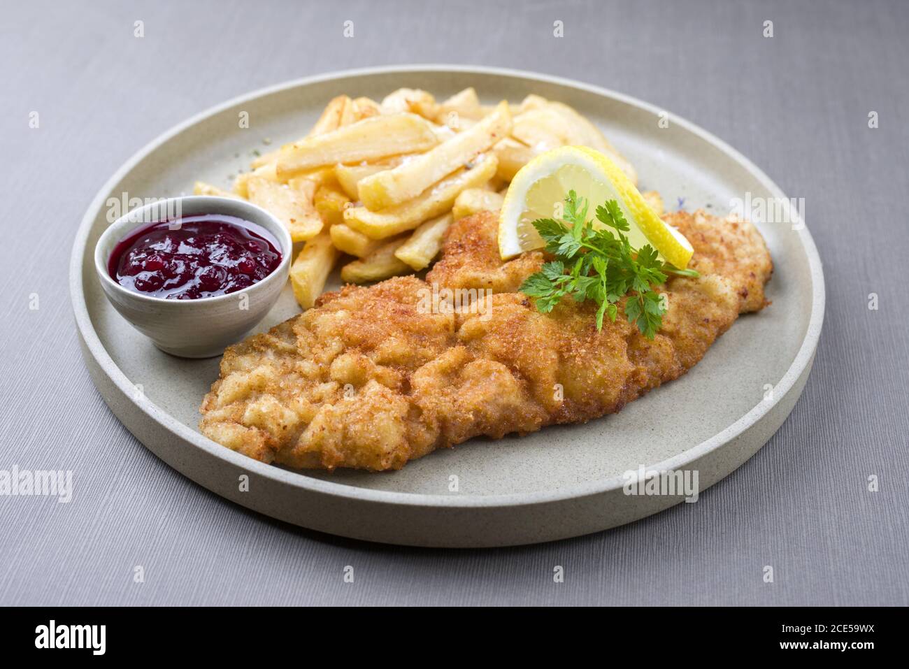 Gebratenes Wiener Schnitzel aus Kalbtopside mit Pommes frites und Preiselbeersoße als Closeup moderner Design-Teller Stockfoto