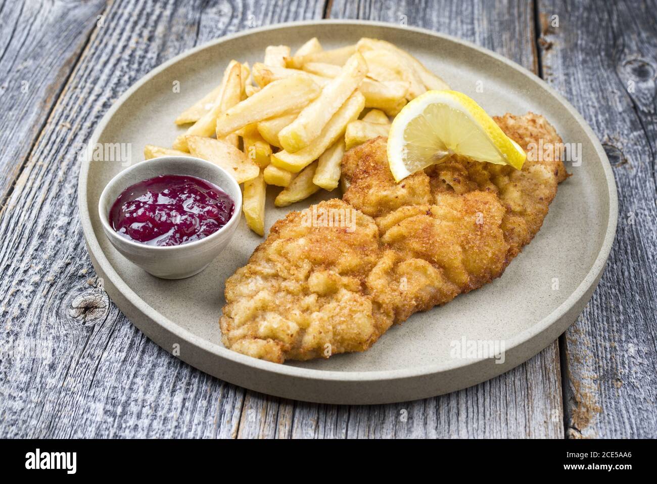 Gebratenes Wiener Schnitzel aus Kalbtopside mit Pommes frites und Preiselbeersoße als Closeup moderner Design-Teller Stockfoto