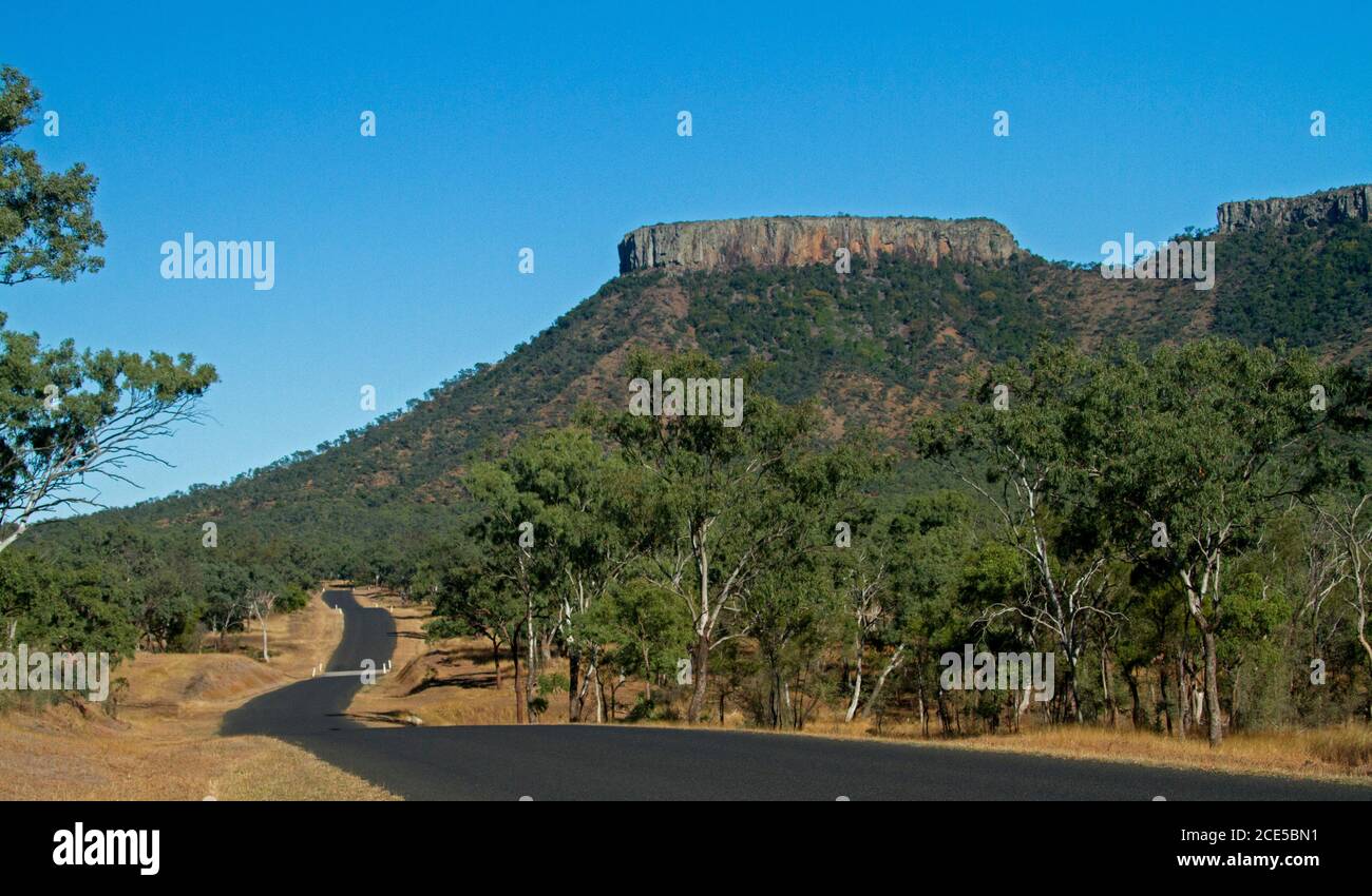 Lords Tafelberg im Peak Range National Park steigt in Blauer Himmel mit Straße, die durch den Vordergrund schlängelt, bedeckt von Bäumen Im Outback Australien Stockfoto