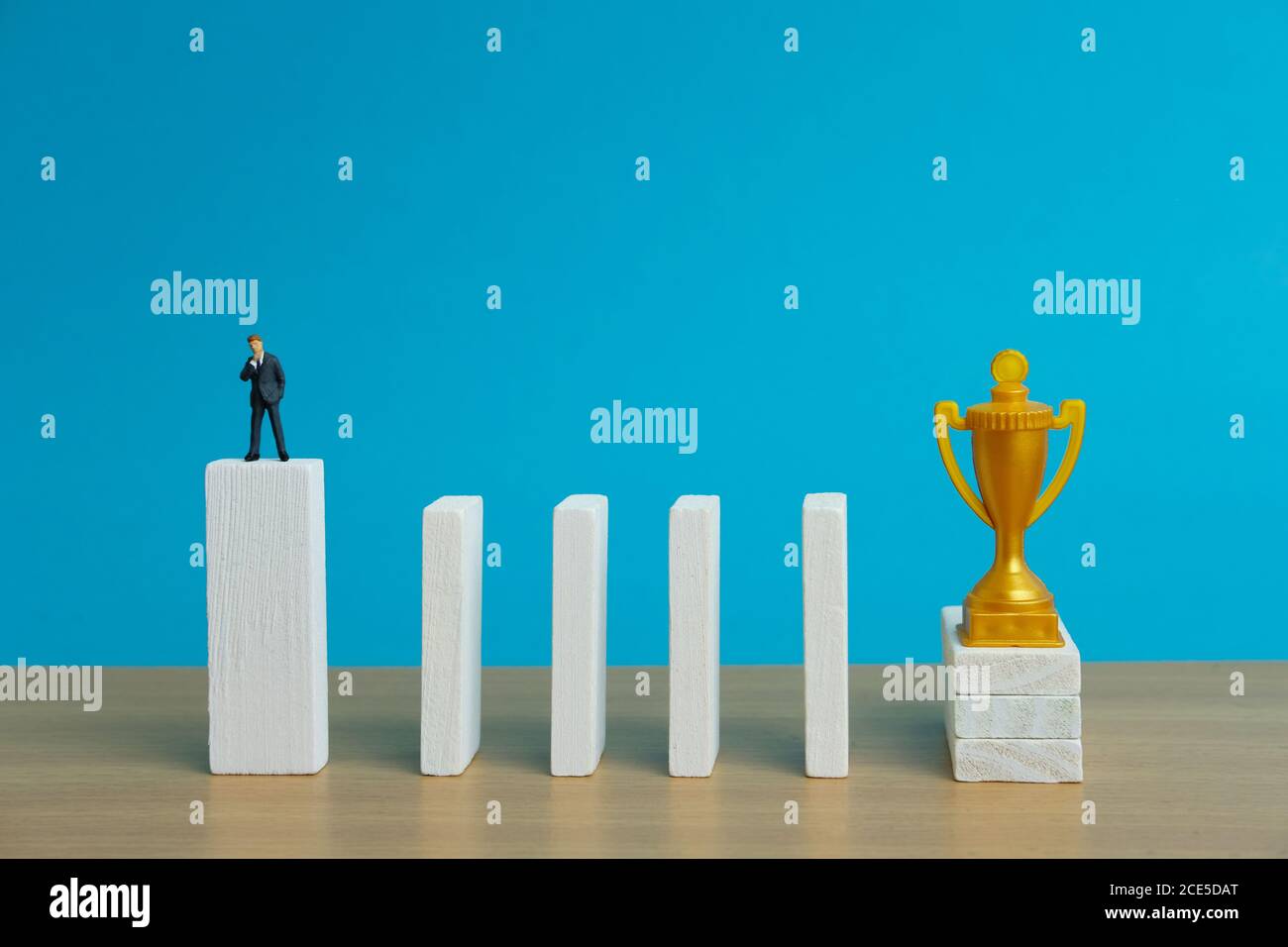 Miniatur Business-Konzept - Geschäftsmann denken vor Hindernis Wand, um goldene Trophäe zu erreichen Stockfoto