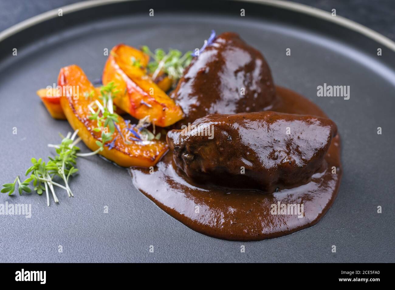 Traditionelle deutsche geschmorte Rinderbacken in brauner Rotweinsauce Mit Kürbisscheiben und Kräutern als Nahaufnahme in einem angeboten Modernes Design Stockfoto