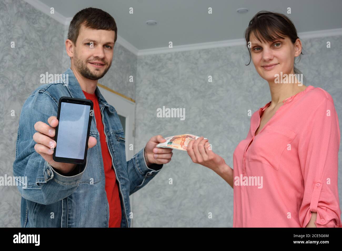 Ein selbstständiger Mann erhält Geld von einem Mädchen für die Reparatur eines Zimmers und zeigt ein Telefon mit der mobilen Anwendung Stockfoto