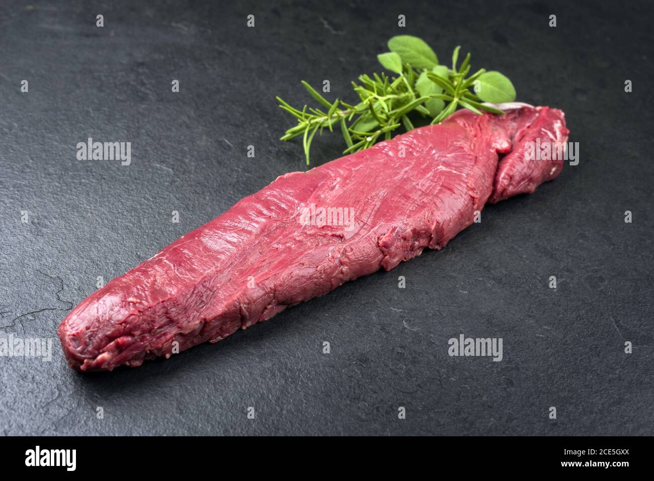 Rohes, trocken gereiftes Wildfilet Steak natürlich mit Kräutern Angeboten als Nahaufnahme auf einem modernen Design-Board Stockfoto