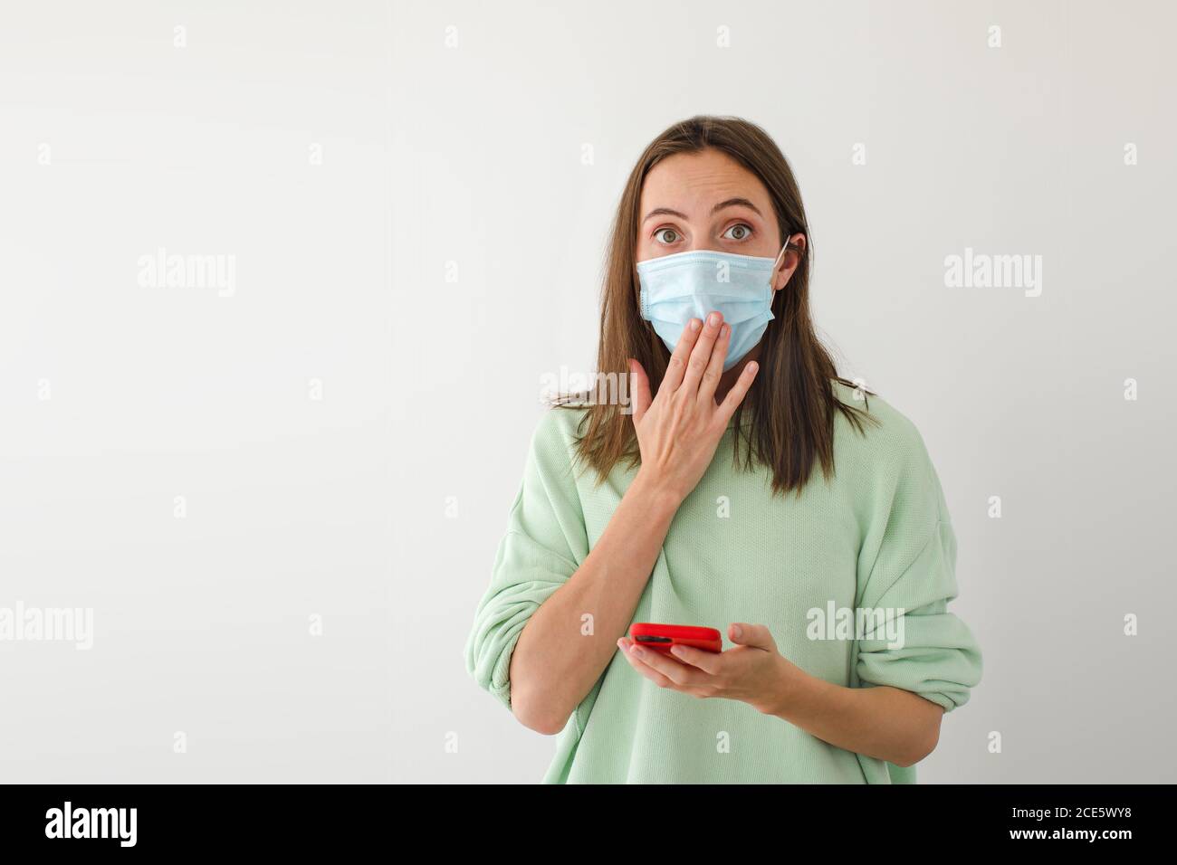 Schockierte Frau in Maske mit Smartphone Stockfoto