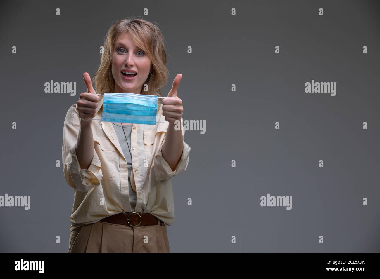 Kopf Porträt attraktive blonde Frau Blick auf Kamera halten medizinische Oder chirurgische blaue Gesichtsmaske Stockfoto