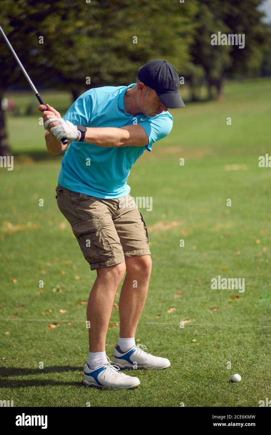 Der Mann, der Golf spielt, schwingt beim Ball, während er spielt Sein Schuss mit einem Eisenklub von hinten betrachtet Auf dem Fairway in einem gesunden aktiven Livestyl Stockfoto