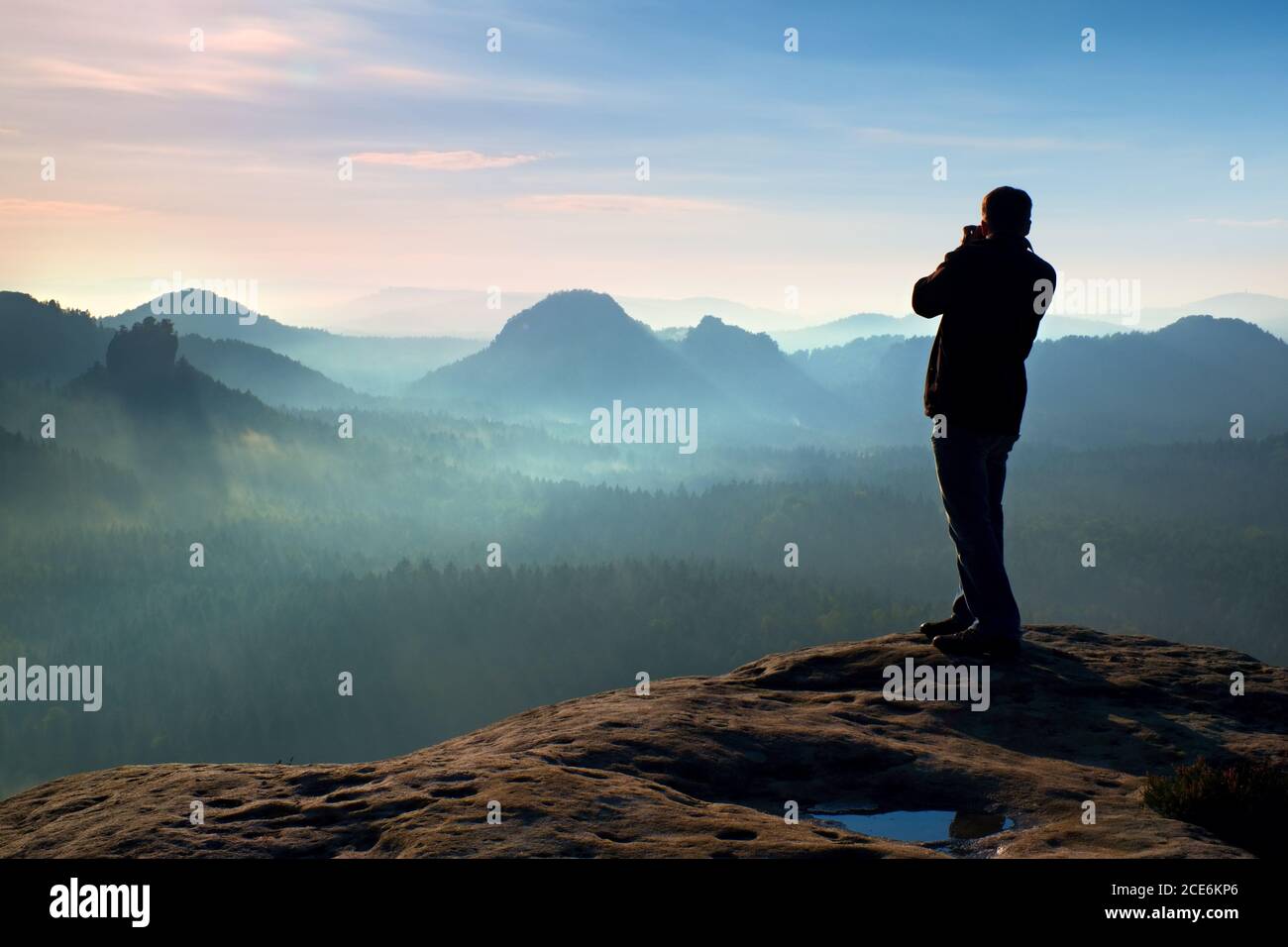 Professioneller Fotograf macht Fotos mit großer Kamera auf Felsen. Gefährliche Lage am Ende der Klippe. Verträumte neblige Landschaft, h Stockfoto