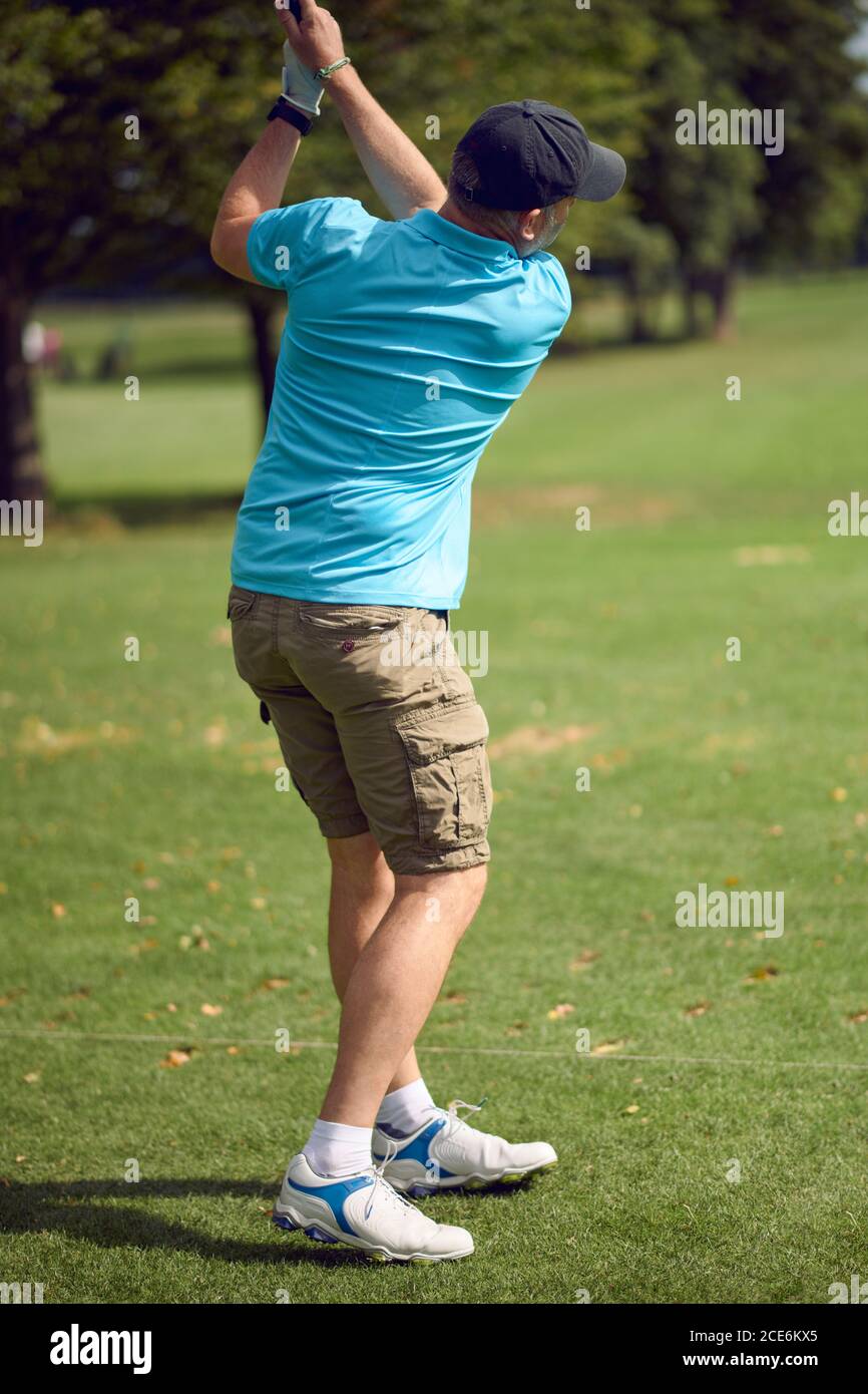 Der Mann, der Golf spielt, schwingt beim Ball, während er spielt Sein Schuss mit einem Fahrer von hinten gesehen Blick nach unten Das Fairway in einem gesunden aktiven Lebensstil Co Stockfoto