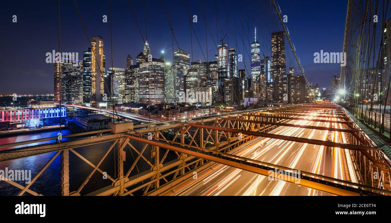 Panoramablick auf die Wolkenkratzer von Lower Manhattan bei Dusk und Brooklyn Bridge mit leichten Wanderwegen. Abend in New York City, NY, USA Stockfoto
