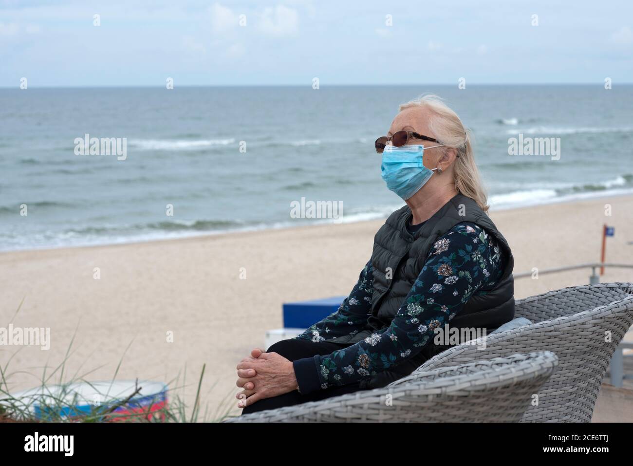 Ältere Frau mit Schutzmaske am leeren Strand. Stockfoto
