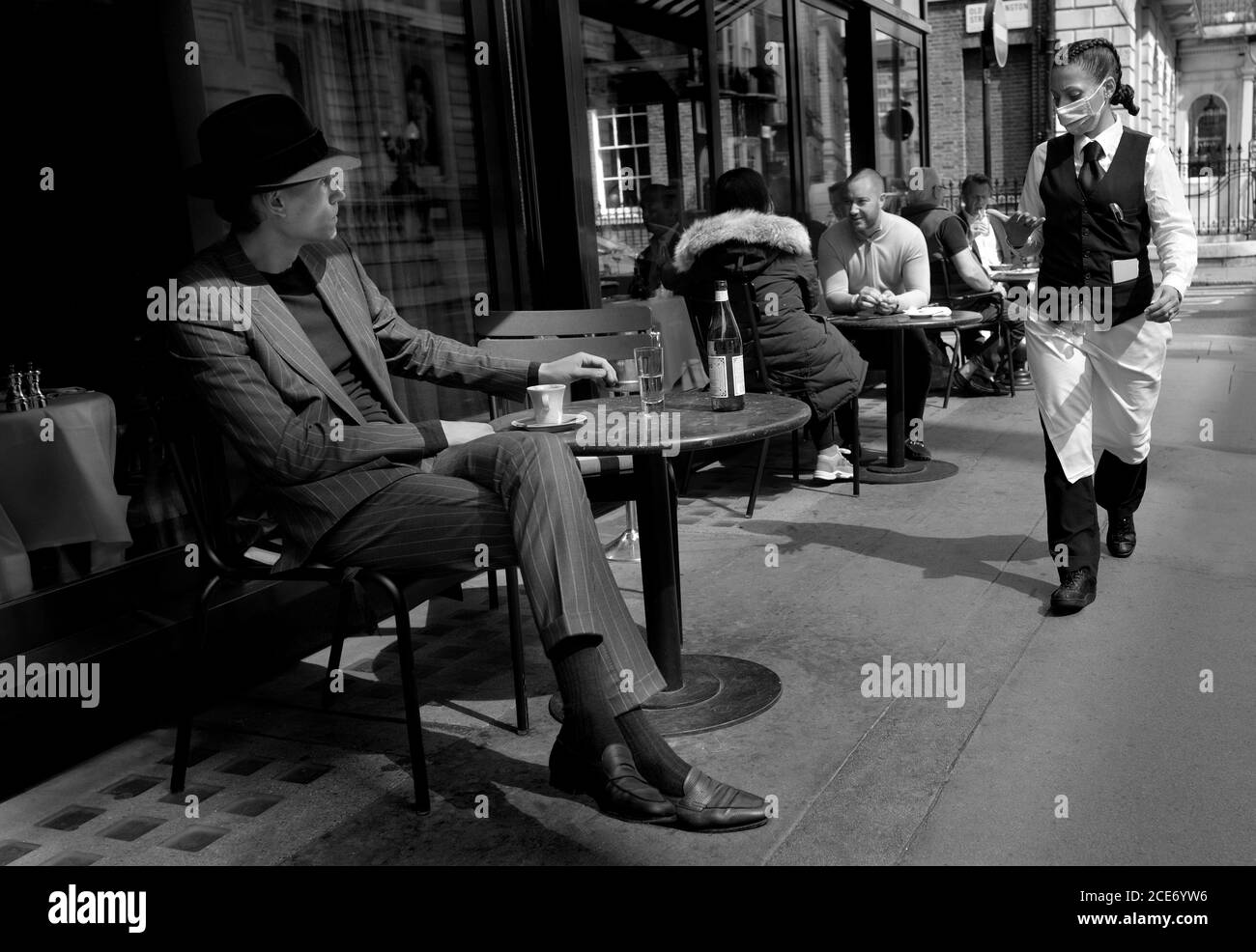 London, England, Großbritannien. Mann sitzt vor einem Café - Kellnerin trägt eine Gesichtsmaske, während der COVID Pandemie, August 2020 während der COVID Pandemie, Augus Stockfoto