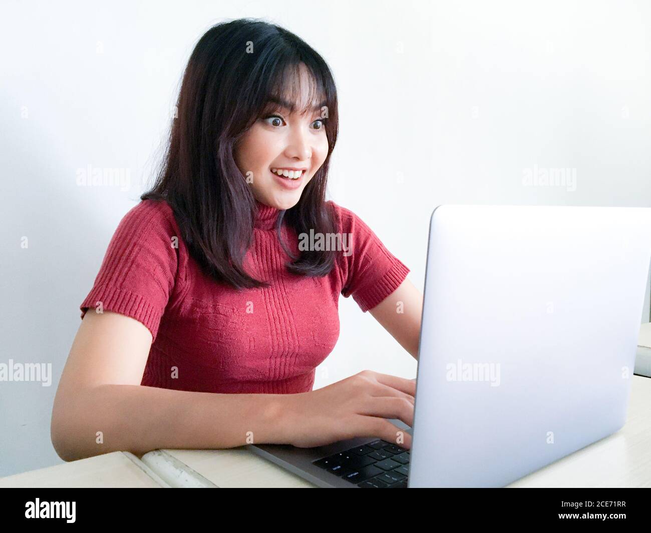 Asiatische Frau tragen rotes Hemd mit Laptop Gefühl aufgeregt schreit vor Freude und Glück, Überraschung, Gewinner Ausdruck, weißer Hintergrund. Indonesische Frauen Stockfoto