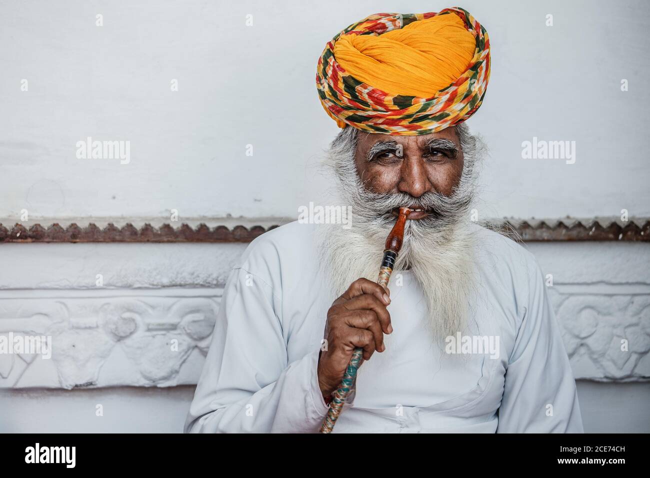 Indien - 30. Oktober 2012: Inhalt älterer indischer Mann in traditionellem Turban sitzt in der Nähe von Steingebäude und raucht Shisha, während er sich entspannt und wegschaut Stockfoto