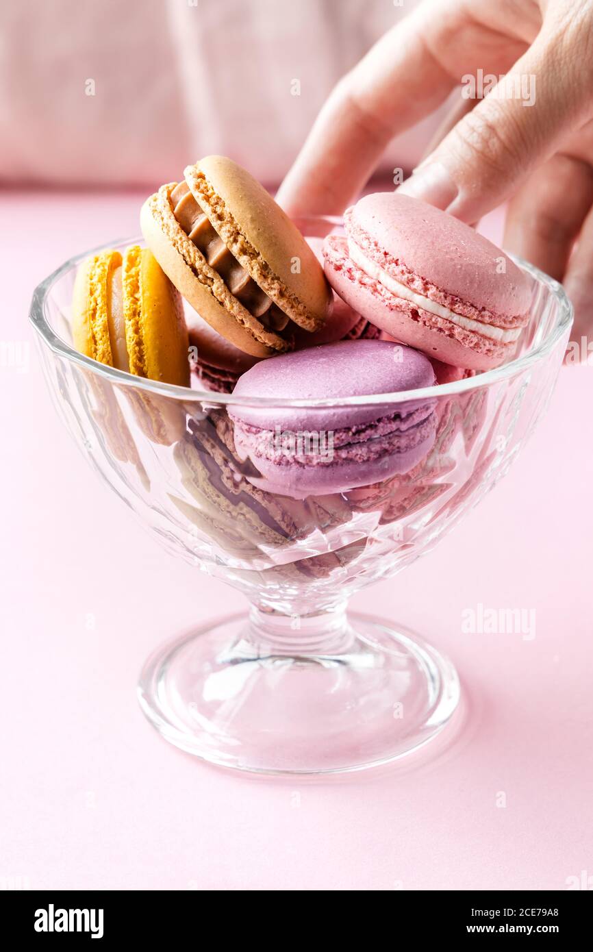 Crop weiblich unter bunten leckeren Macarons aus Glas Schüssel platziert Auf dem Tisch in der Küche Stockfoto
