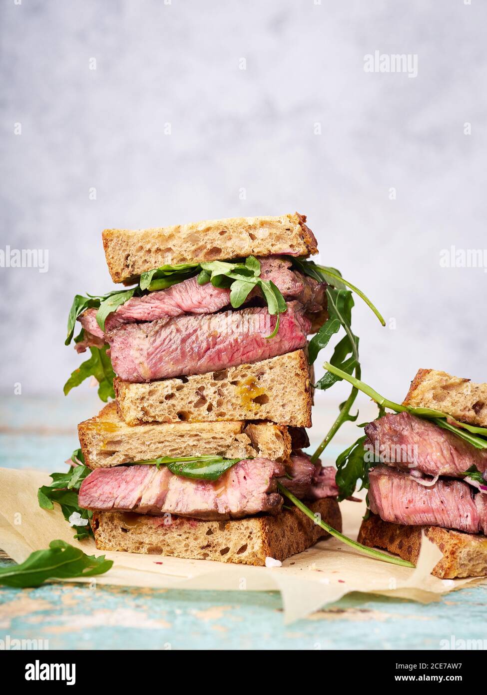 Nahaufnahme eines Stapels Rindersteak Sandwich mit Rucola und Senf Dressing vor hellem Hintergrund Stockfoto