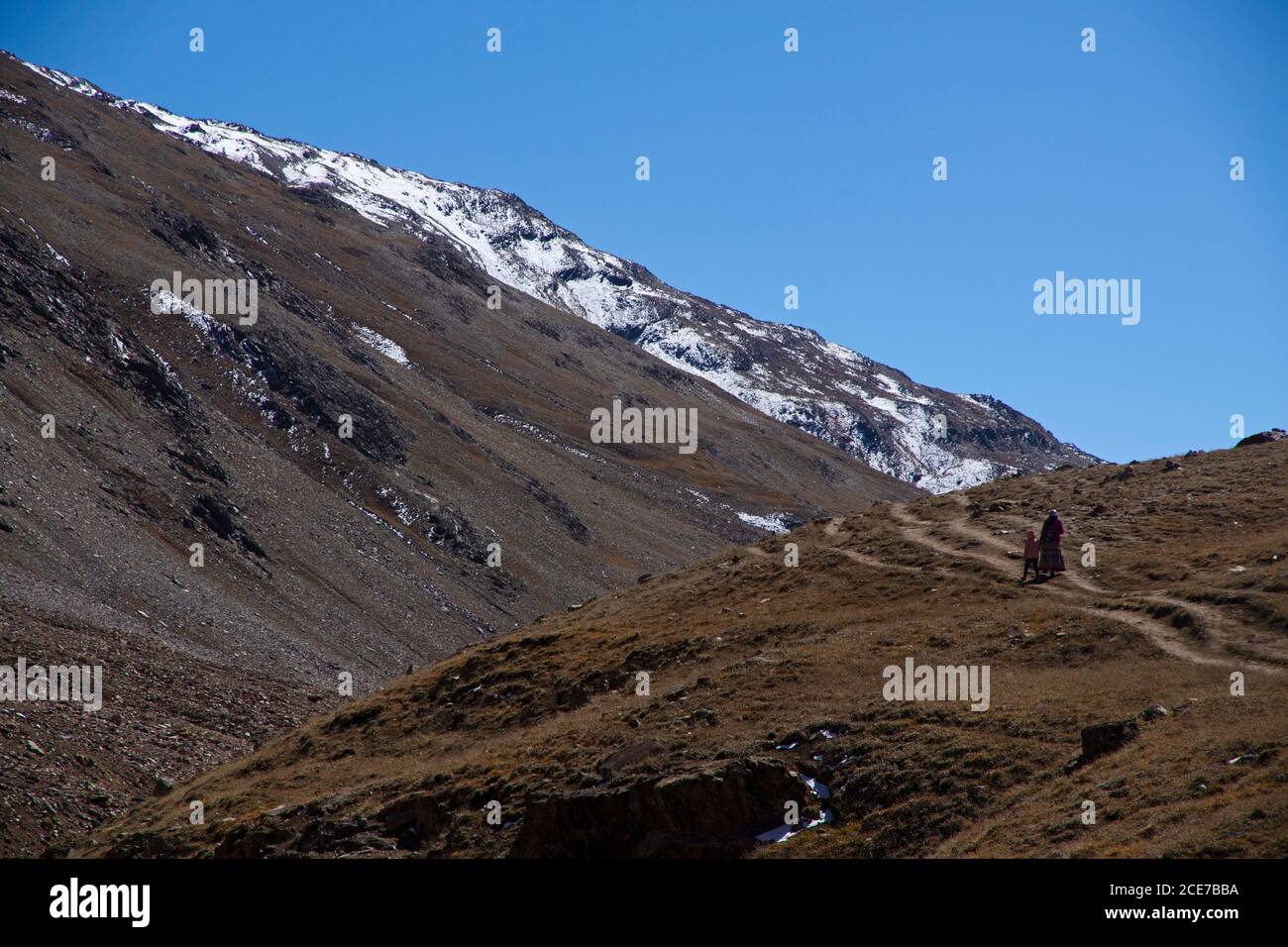 Zwei Personen - Touristen - eine Mutter und ein Kind gehen auf einem schmalen Weg auf einem Hügel in der Nähe Chandratal an einem klaren Tag mit blauem Himmel. Stockfoto