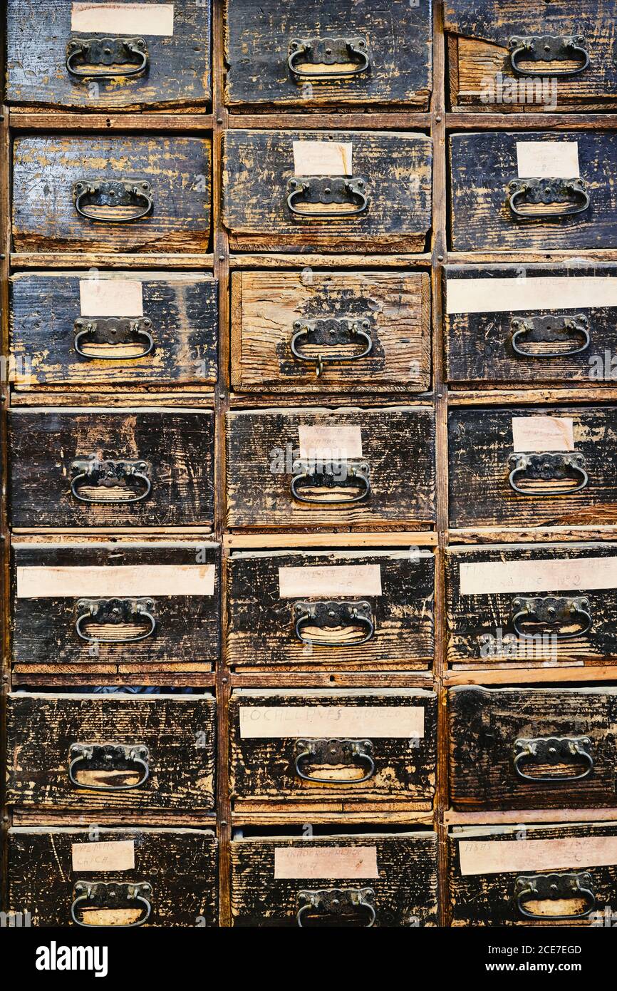Archiv, das identische dunkelbraune Holzschubladen mit rechteckigen Griffen darstellt Mit Flecken und Worten in der Werkstatt Stockfoto