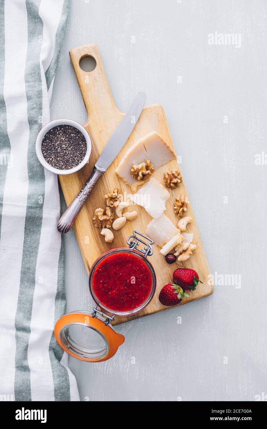 Von oben Blick auf den Tisch mit Erdbeermarmelade in einem Glas, Käse in Scheiben und Käse auf Holzbrett serviert Stockfoto