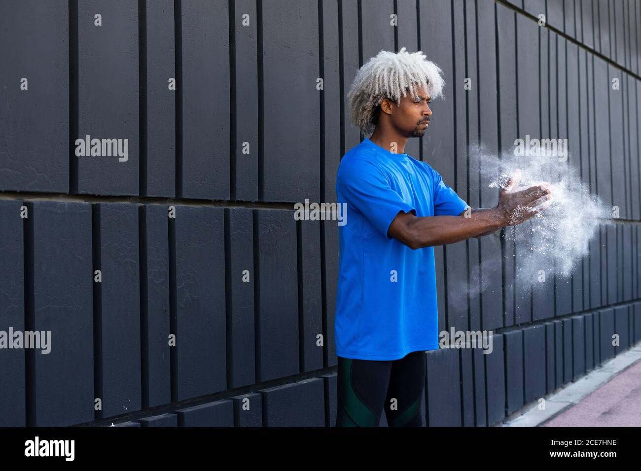 African American männlichen Athleten mit gefärbten Haaren klatschen Hände mit Kreidepulver während der Vorbereitung für das Training in der Nähe Wand der modernen Gebäude Stockfoto