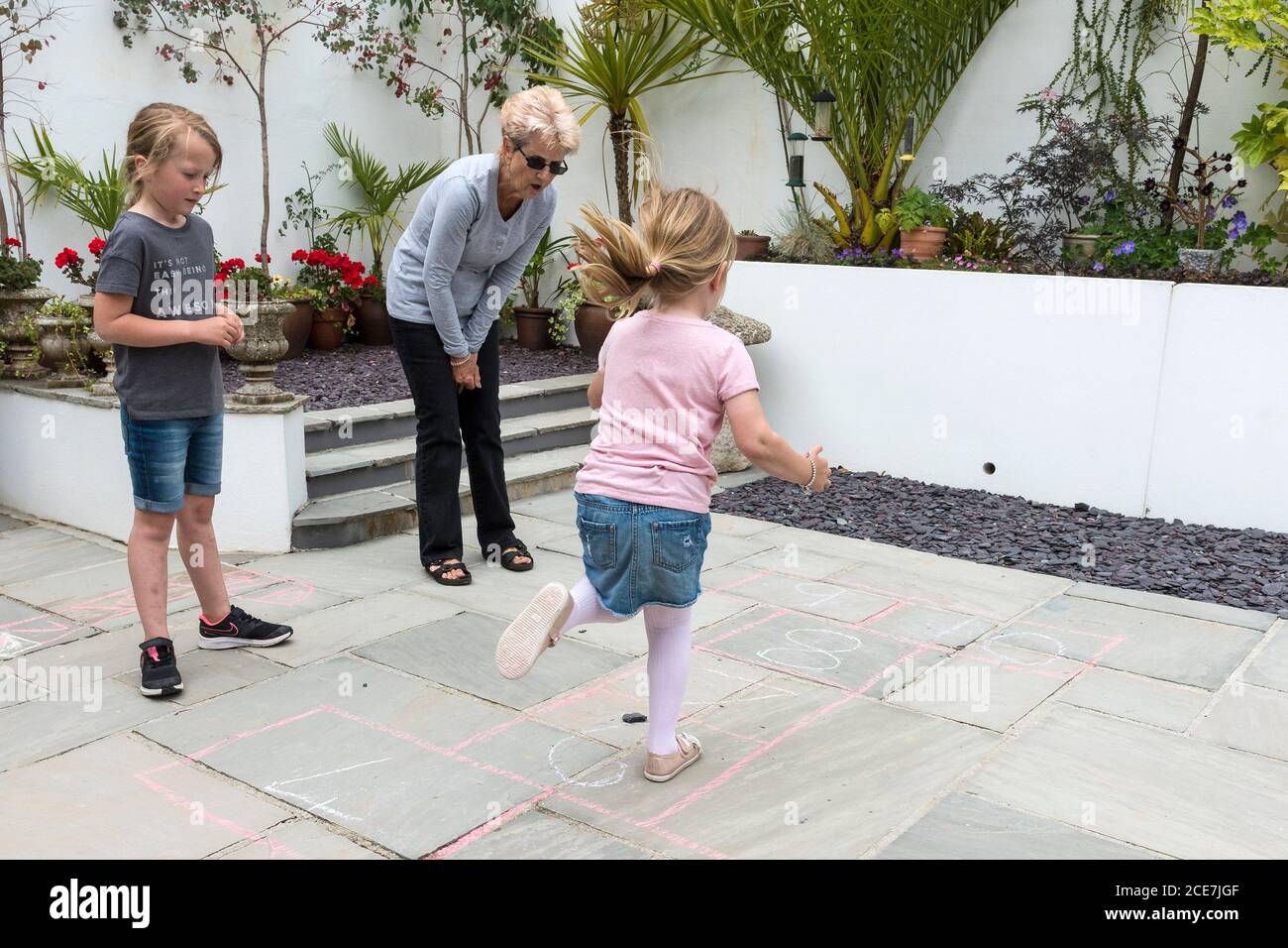 Eine Großmutter lehrt ihre Enkelinnen ein traditionelles Spiel von hopscotch. Stockfoto