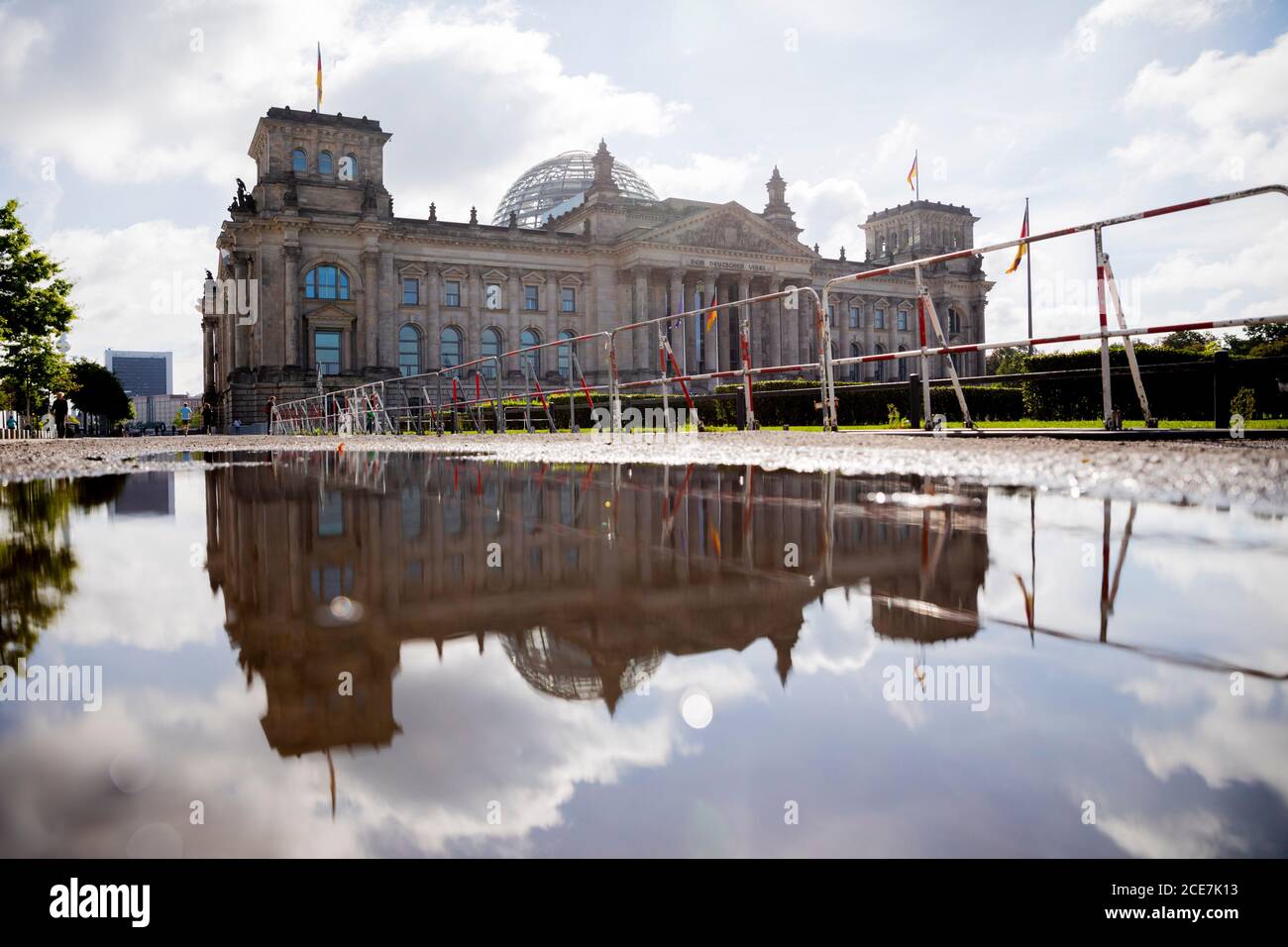 Berlin, Deutschland. August 2020. Das Gebäude des Reichstags spiegelt sich in einer großen Pfütze des Regens auf einem Sperrzaun wider. Zwei Tage zuvor stürmten Demonstranten mit Reichsflaggen und rechtsextremistischen Schimpfungen auf die Treppe des Reichstags und nur drei Polizisten hielten die wütende Menge mit winkenden Schlagstöcken fern. Quelle: Christoph Soeder/dpa/Alamy Live News Stockfoto