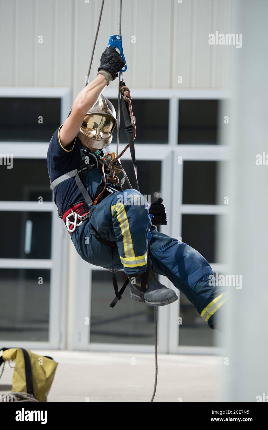 Seitenansicht eines starken Feuerwehrmann in Schutzausrüstung während des Trainings Mit Seilen in der Nähe des Gebäudes Stockfoto