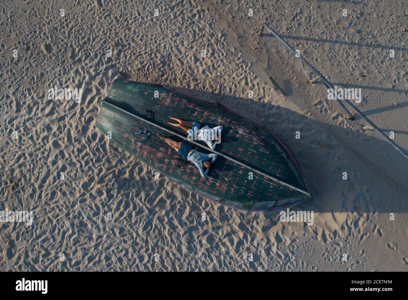 Drone Ansicht Ganzkörper gesichtslosen Paar in lässigen Sommer tragen Entspannen mit Kopf auf Händen auf hölzernen Ruderboot umgedreht Unten am Sandstrand Stockfoto
