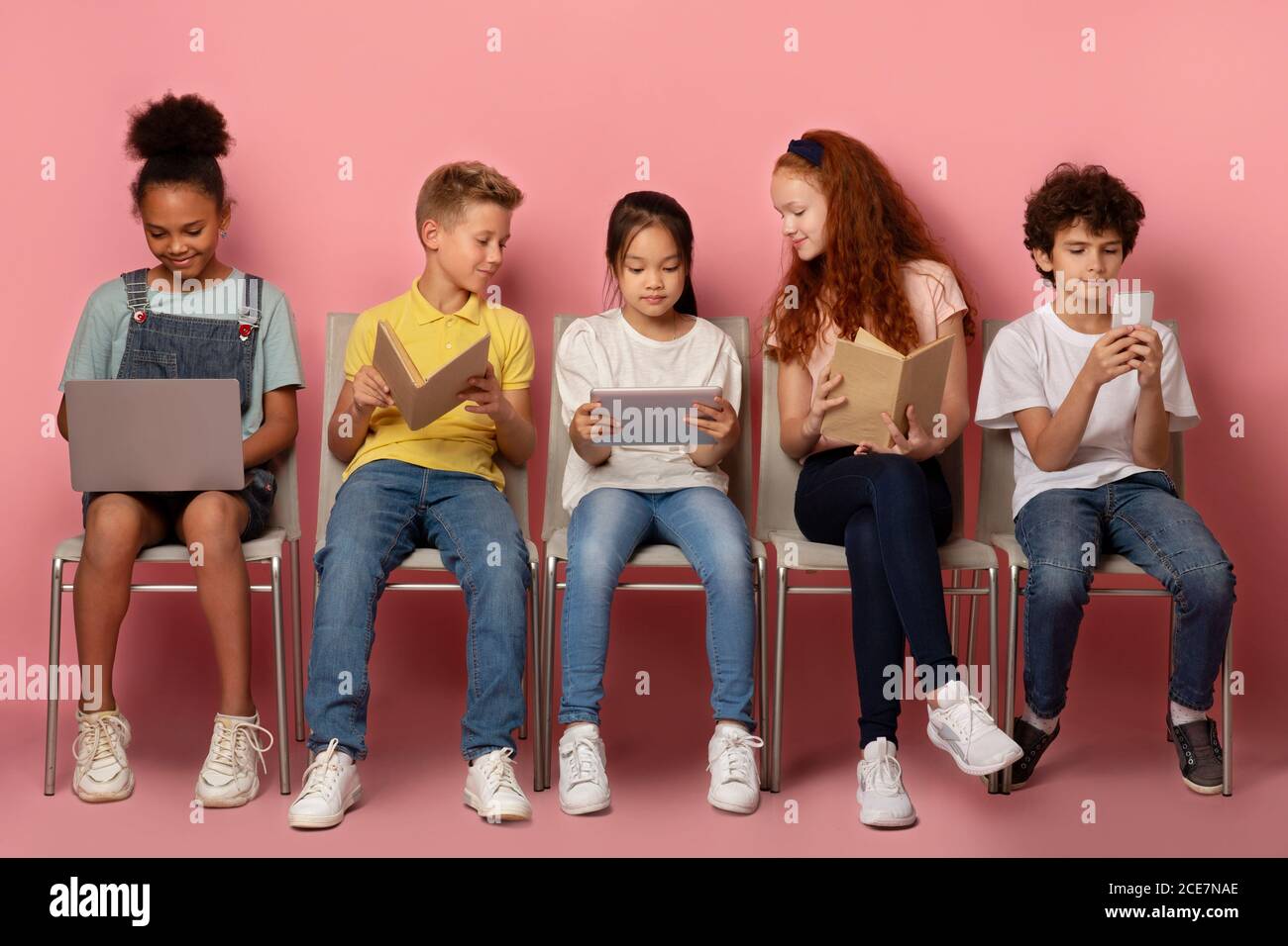 Diverse Schulkinder mit Tablet, Laptop, Smartphone und Bücher online auf Stühlen über rosa Hintergrund zu lernen Stockfoto