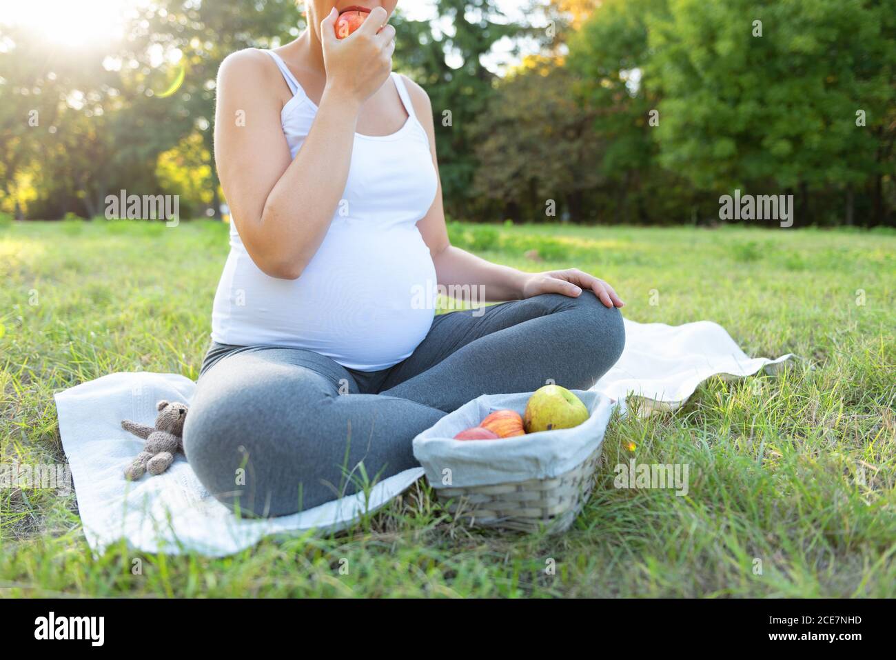 Nahaufnahme einer jungen Frau in Sportkleidung, die auf einer Trainingsmatte sitzt und beim Training im Freien frischen Apfel isst. Erwartet weibliche tun Yoga auf der Stockfoto