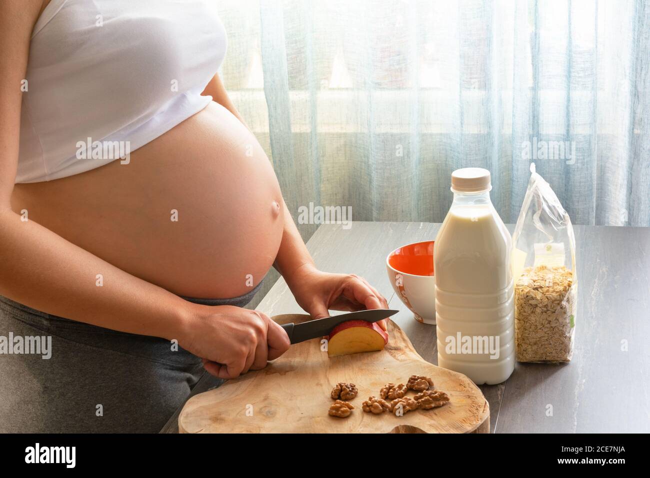 Junge und schöne schwangere Frau bereitet gesundes Frühstück zu Hause. Zugeschnittenes Bild von schwangeren Frau Kochen ein Frühstück mit Haferflocken, Apfel, mi Stockfoto