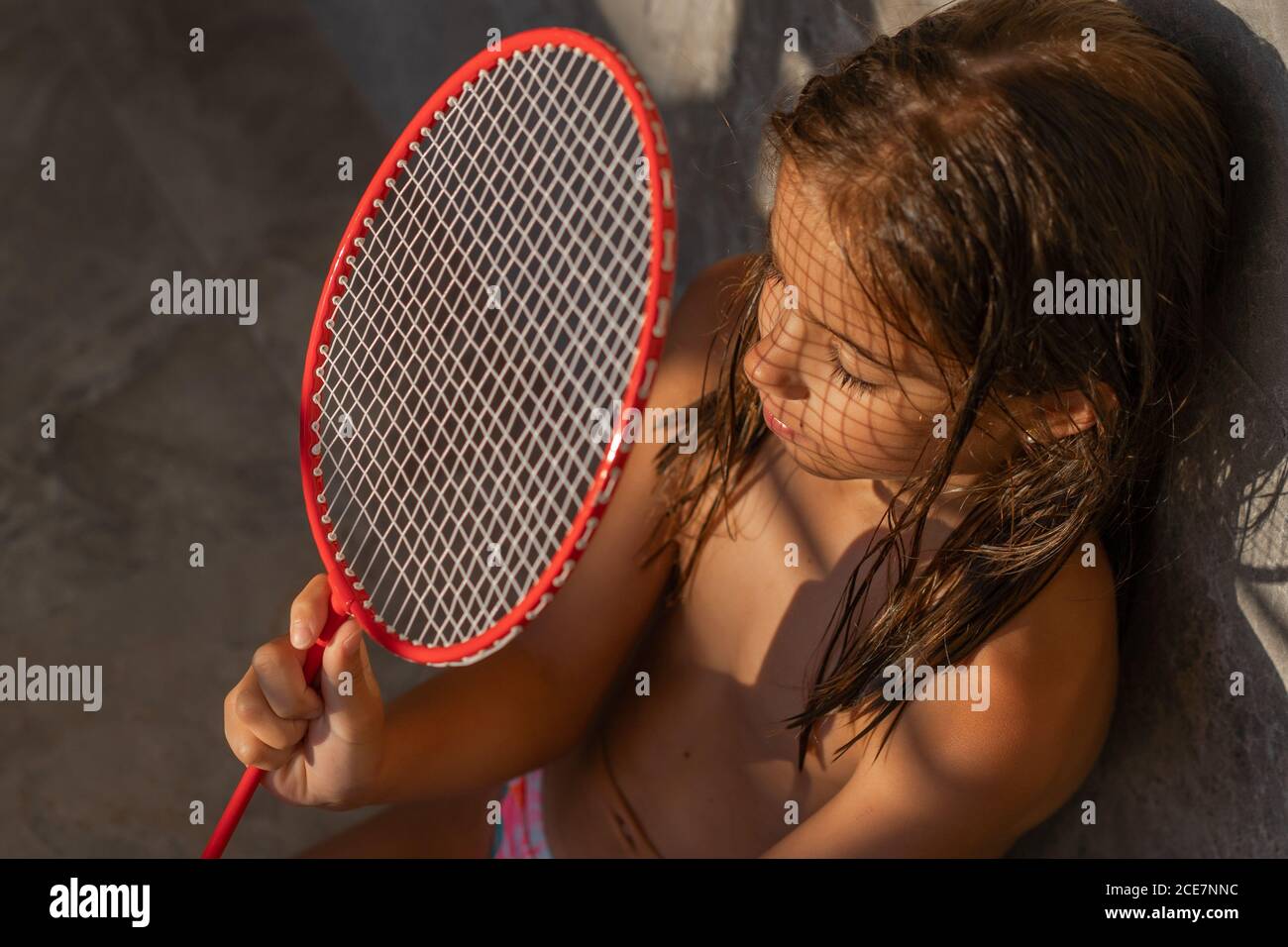 Von oben von ruhigen Kind sitzen im Hinterhof und Bedeckung Gesicht mit Badmintonschläger an sonnigen Tag Stockfoto