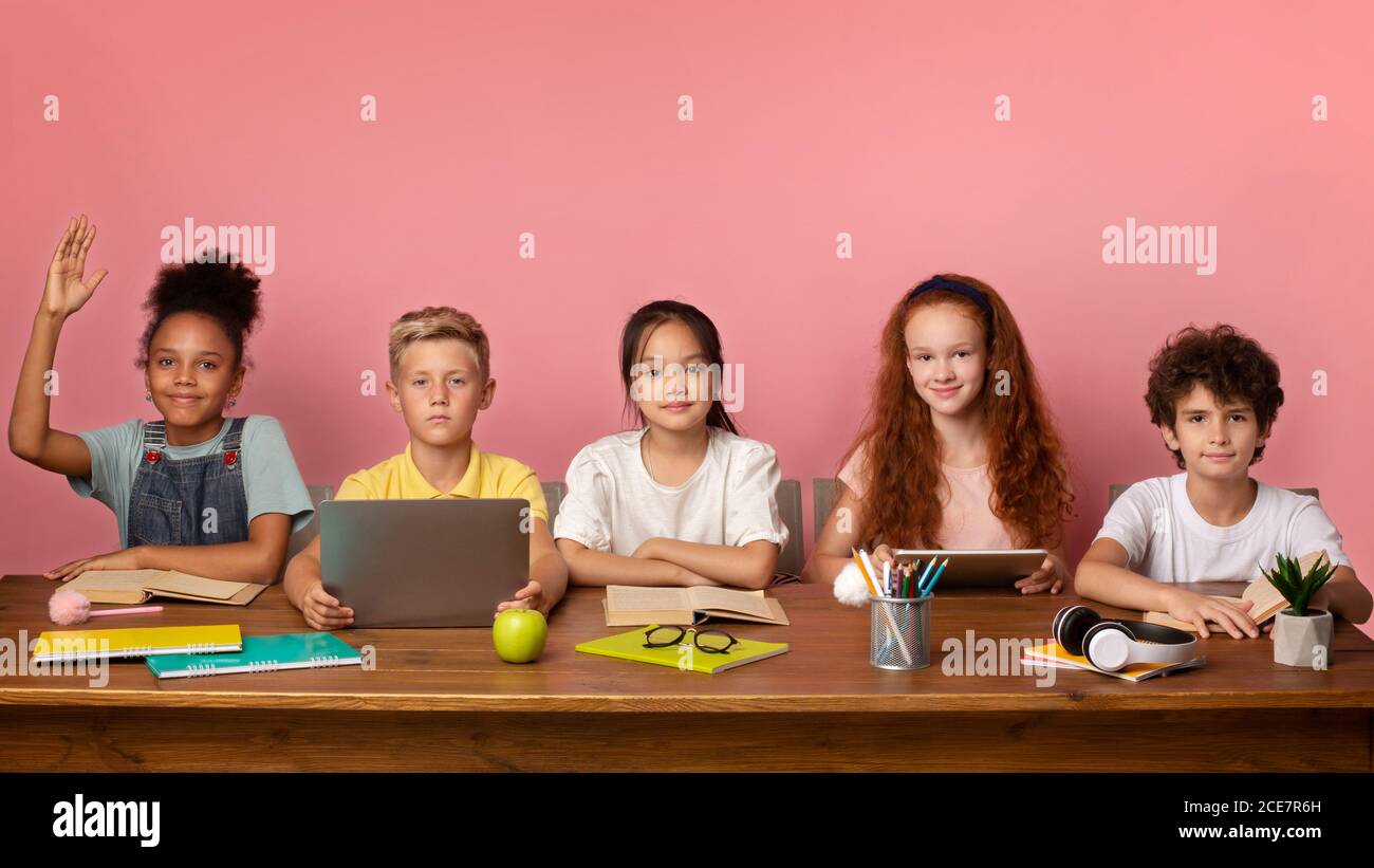 Fokussiertes schwarzes Mädchen und ihre Freunde bereit, Lektion am Schreibtisch über rosa Hintergrund, freien Raum zu beantworten Stockfoto