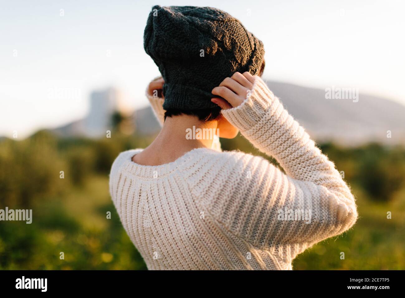 Rückansicht von unkenntlich weiblich in warmen Pullover Anziehen hut und bewundern erstaunliche Sonnenuntergang im Hochland Stockfoto
