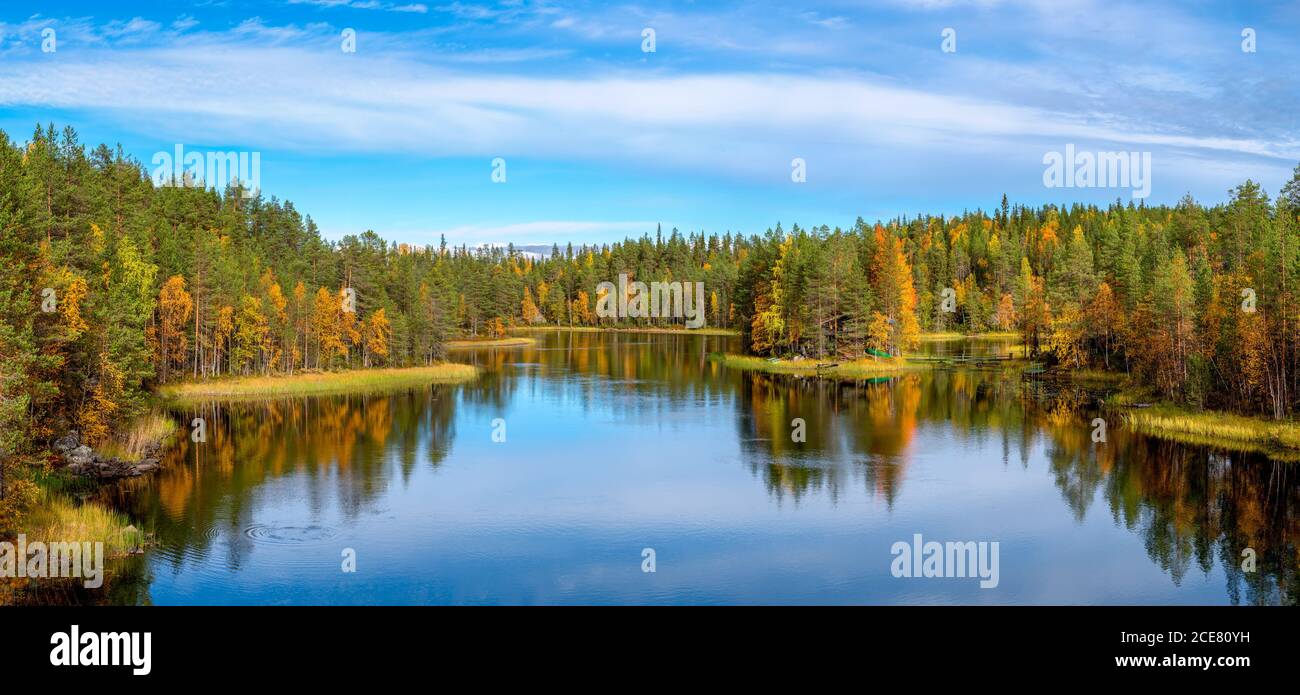 Friedlicher See, umgeben von Wald mit bunten Bäumen, die sich darin spiegeln Wasser gegen strahlend blauen Himmel Stockfoto