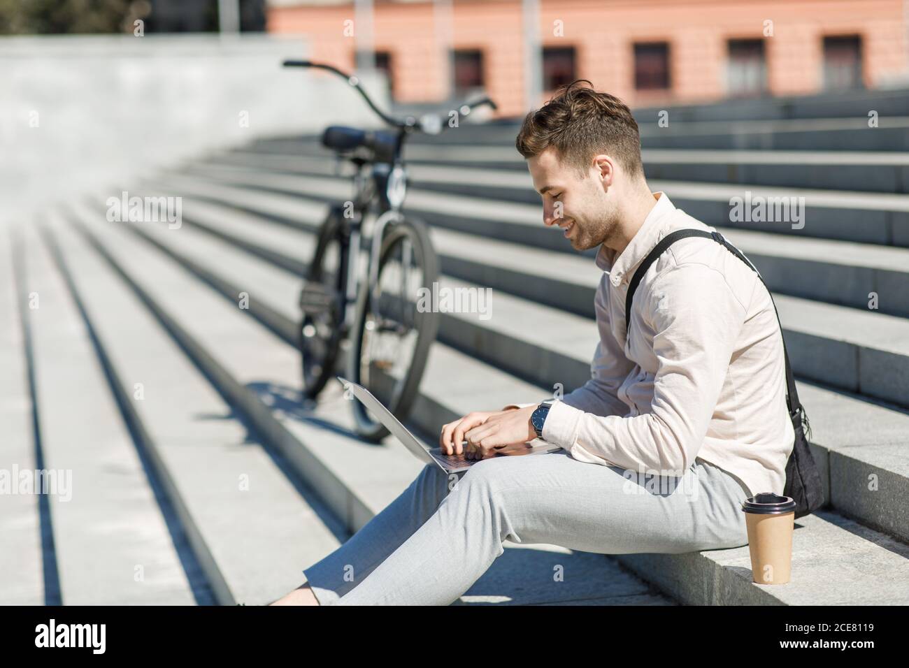 Moderner Mitarbeiter sitzt auf Treppen und Networking im Freien mit Take Away Kaffee und Fahrrad Stockfoto