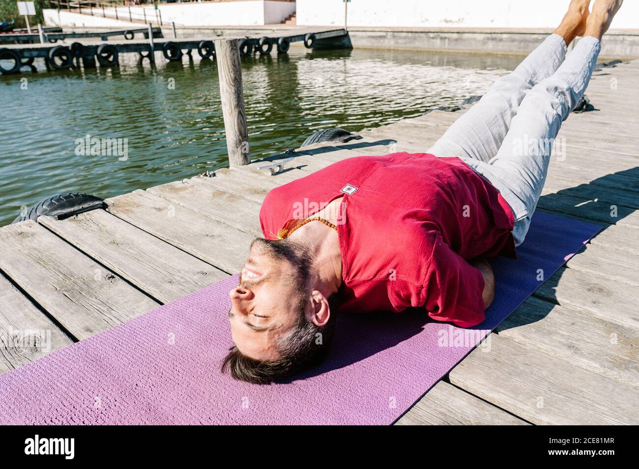 Von oben von ruhigen bärtigen Männchen in lässiger Kleidung Stretching Rückenmuskeln während der Fischvorbereitung Yoga Pose auf Holz pier Stockfoto