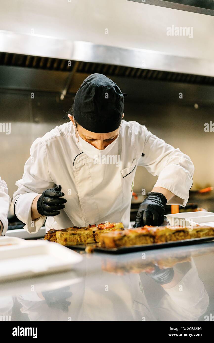 Koch trägt Latexhandschuhe und einheitliche Verpackung lecker gebackenen Quiche In Takeaway-Behälter für die Lieferung in der Caféküche Stockfoto