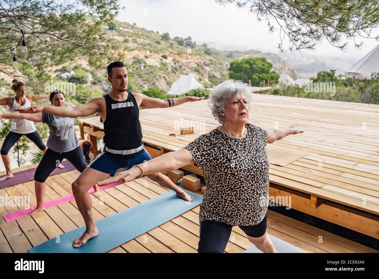 Gruppe von motivierten Tauchern in verschiedenen Altersstufen, die Beine strecken Und Knöchel während der Durchführung Virabhadrasana B Pose während Outdoor-Yoga Klasse Stockfoto